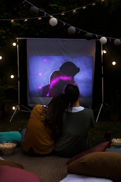 A close-up of a portable projector displaying a clear and bright image on a white screen in a darkened outdoor setting. The projector is small and sleek, showcasing its portability.