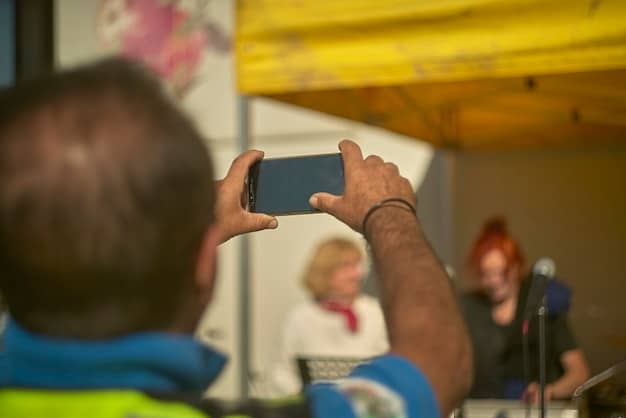 A close-up shot of a diverse hand holding a smartphone, capturing a live news event in a bustling city street, emphasizing the immediacy and accessibility of citizen journalism.