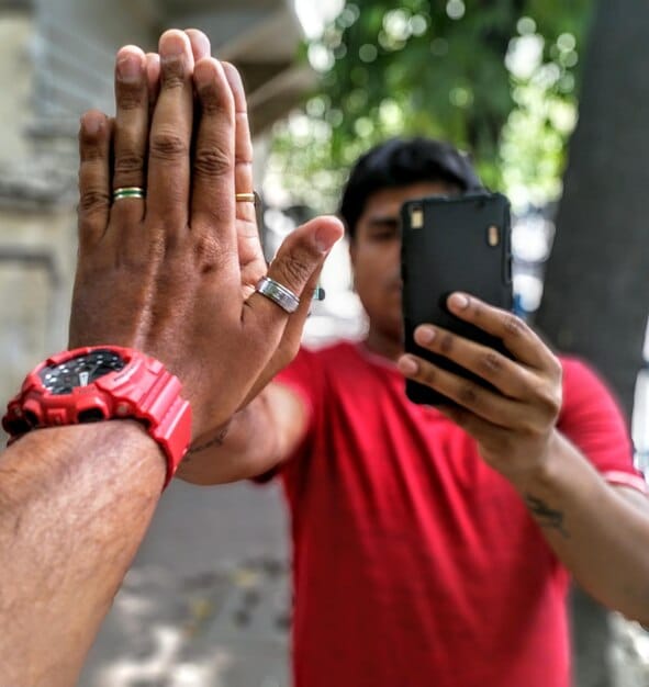 A close-up shot of a person's hands holding a smartphone, recording a protest or community event. The background is slightly blurred, emphasizing the person and their phone as the focal point. The screen of the phone displays a recording interface, suggesting live reporting.