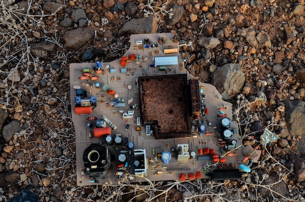 A close-up shot of corroded electronics components in a landfill, highlighting the presence of heavy metals and toxic chemicals. The image is intended to emphasize the environmental hazards associated with improper e-waste disposal.